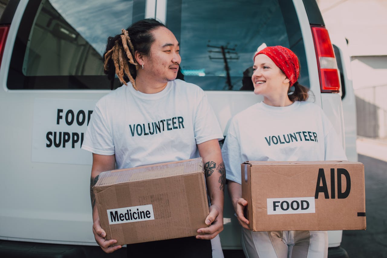 why-choose-us Two smiling volunteers carrying boxes labeled food and medicine by a supply van.